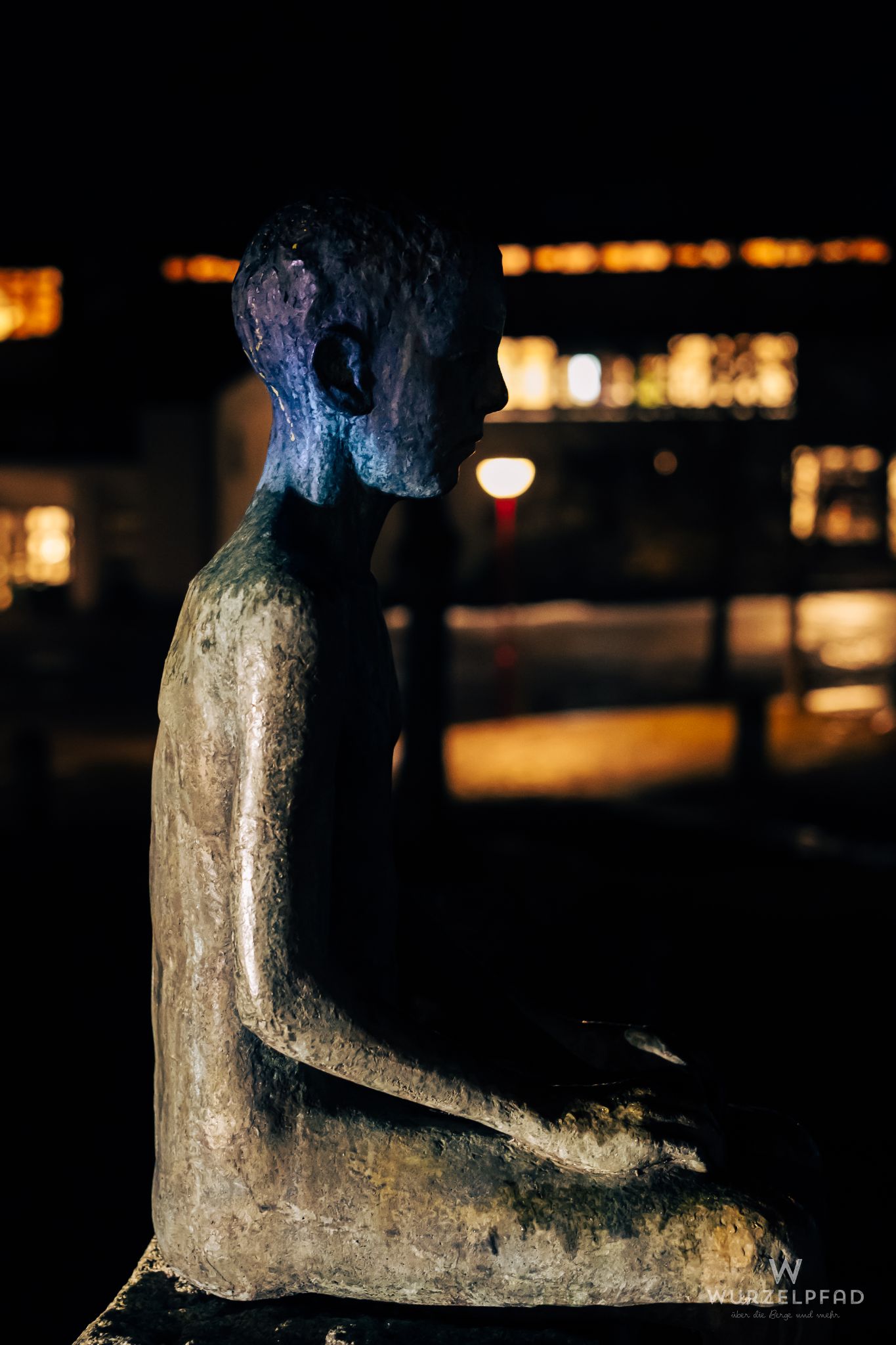 Bronzefigur eines sitzenden Kindes im Profil bei Nacht, mit vers