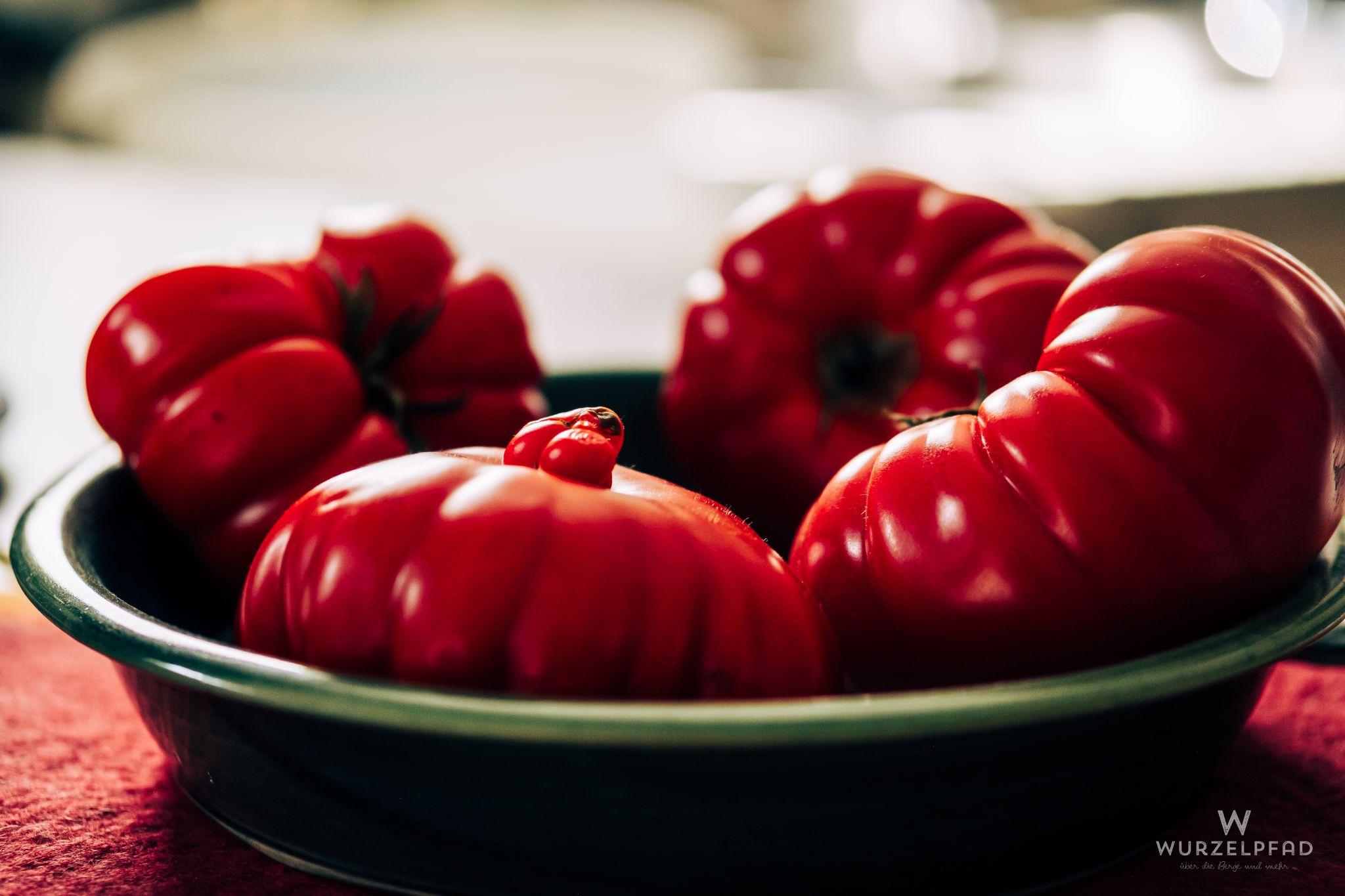 Vier rote Ochsenherztomaten in einer dunkelgrünen Schale